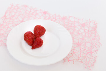 three red strawberries on a white plate on the pink  decoration mesh the white background