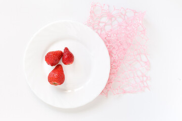 three red strawberries on a white plate on the pink  decoration mesh the white background