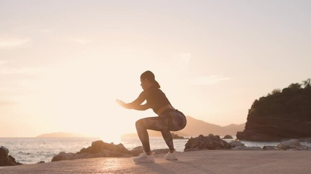 sporty woman squats workout on beach. Beautiful fitness model butt workout outdoors. Sunset beach with sea view background.