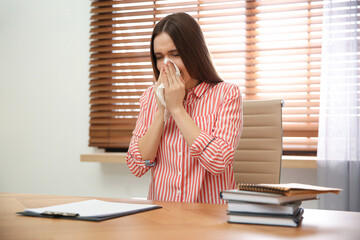 Sick young woman sneezing at workplace. Influenza virus