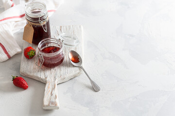 Sweet homemade strawberry jam in glass jars and fresh berries on white wooden board on rustic white background. Copy space. Cookbook recipe. Social media content. Summer strawberry confiture