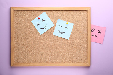 Cork board and paper notes with drawn faces on violet background. Concept of jealousy