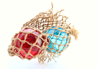 Red and blue glass net floats in traditional netting. Used to keep fishing nets afloat. Coastal home image or industrial image showing this traditional fishing method. © Scorsby
