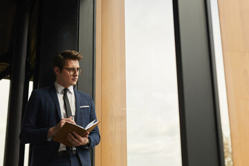 Fototapeta premium Waist up portrait of business agent holding notebook standing by modern house and looking away, copy space