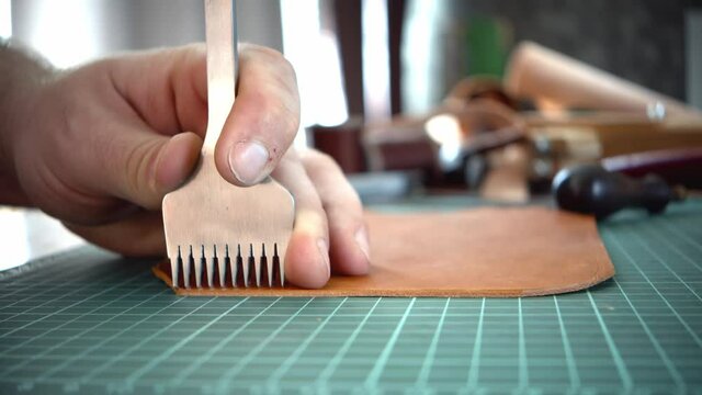 A man's hand holds a piercer punches on a piece of leather and punches a hole with a hammer. Processing the edge of the skin with a special tool, a hole punch for the skin