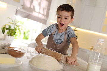 Emotional little boy rolling dough at table in kitchen. Cooking pastry