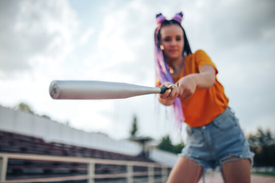 Young beautiful girl holding a baseball bat in a yellow open-air t-shirt in a sports stadium