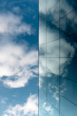 Fototapeta na wymiar A blue sky and a modern blue glass facade in which clouds are reflected.