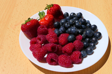 White plate with mixed berries including strawberries, raspberries and blueberries on a wooden table