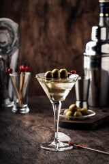 Martini cocktail, with dry vermouth, vodka and green olives, vintage wood bar counter with bar tools