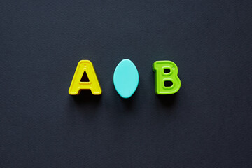 Yellow and green letters A and B uppercase with blue oval object in the middle. Capital letters A and B isolated on black background; copy space, top view