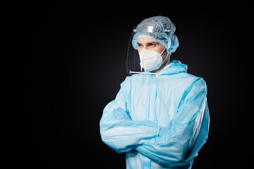 Photo of serious professional guy expert doc virologist arms crossed look empty space wear face mask sterile hazmat blue uniform suit plastic facial shield isolated black color background