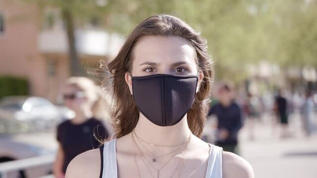 Portrait of a young woman with a black face mask in a crowded harbour.