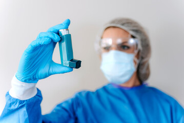 Female doctor holding asthma inhaler on color background, closeup. Medical object.