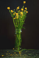 Yellow wildflowers in glass pot on a wooden table