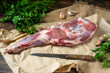 Raw mutton leg on a bone on parchment on a brown wooden table. Sheep meat close-up. A fresh piece of lamb meat is on the table. Top view with space for text	