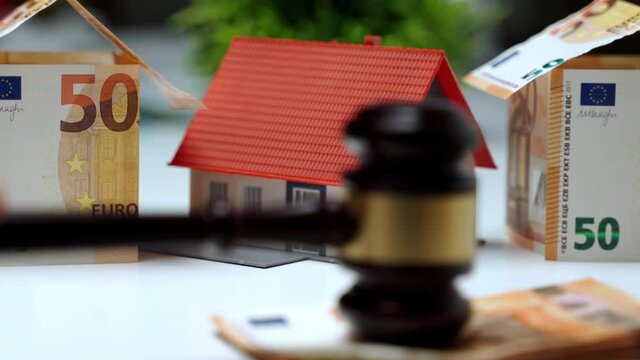 Property auction concept, selling and buying house process with banging judge gavel. Scene of small plastic house among euro banknotes, and judge pounding gavel on stack of money. Real estate auction