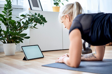 Athletic woman practicing at home with online training on digital tablet doing plank exercise