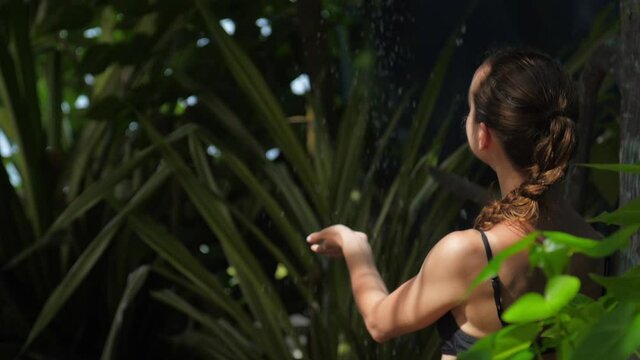 young girl with ponytail turns on refreshing shower after long swimming in ocean backside view slow motion. Concept excotic resort environment