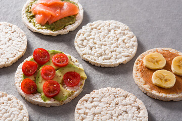 Puffed rice cakes with guacamole salmon,tomato and avocado, and banana with peanut butter on gray stone background