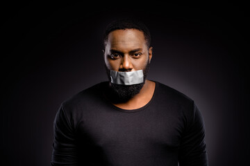Portrait of frustrated voiceless speechless afro american guy have adhesive tape mouth cant speaking racism issue wear sweater isolated over black color background