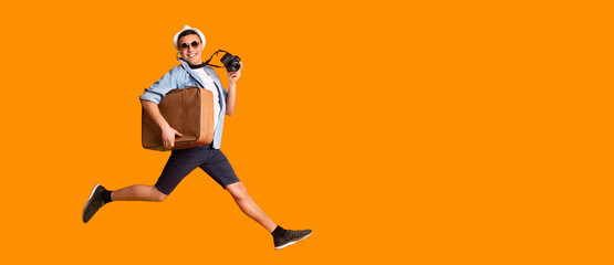 Fototapeta na wymiar Excited young man with camera and suitcase over yellow background
