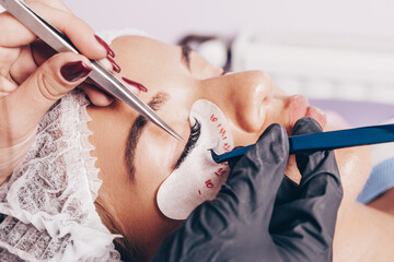 Beautiful young woman getting eyelash extension procedure. Cosmetics and body care concept.
