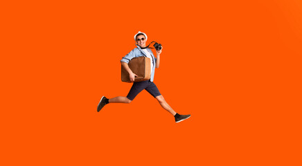 Fototapeta na wymiar Happy photographer with suitcase running fast over orange background