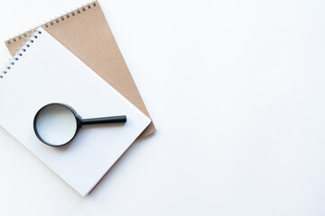 Workplace with notebooks and magnifying glass on the left on light white backround. Copy space. Top view. Concept business.