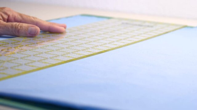 Woman tailor cutting blue cotton fabric using a rotary cutter on a cutting pad. Hand holding a ruler as a knife cuts a piece of fabric.