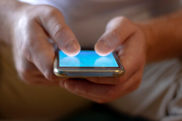 Shot of unrecognizable man using phone at home.Man siting and texting on smartphone.Modern new phone in hands of young man.Lifestyle,technology and communication concept.Close up of hands with mobile.