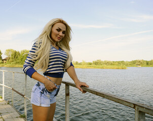 A young girl in jeans shorts and a jacket stands near the lake in nature