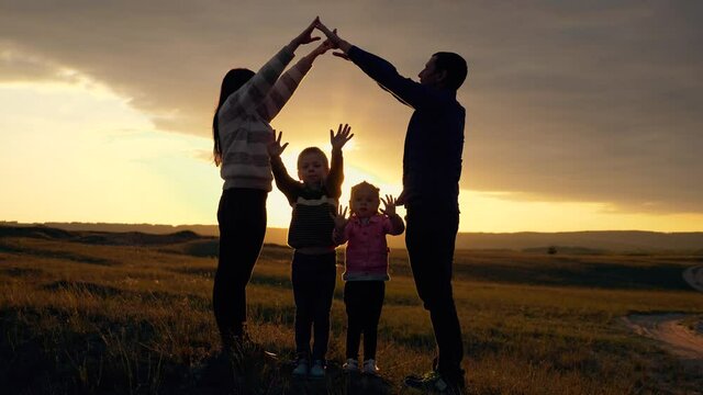 Silhouette of a happy family with young children dreaming of their own home. Parents hold their hands over their children's heads, a symbol of home, home, and child protection.