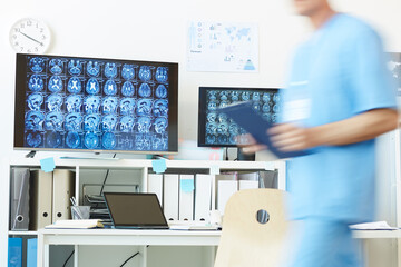 Background image of modern computer equipment with CT brain scans on screens at work station and blurred shape of unrecognizable medic walking in foreground, copy space