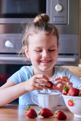 Beautiful European child in the kitchen eating strawberries and drinking milk.