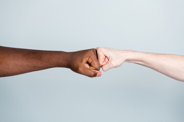 Closeup photo of two arms different race skin colors multinational friends antiracism issue help together buddies world globe integration giving fists bump isolated grey color background
