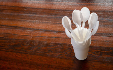 Vasos y cucharas de plástico blanco desechables sobre una mesa de madera oscura