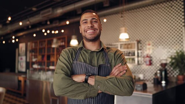 Portrait Of Successful African Male Chef Wearing Black Apron Standing With Folded Arms In Cafe Against Counter