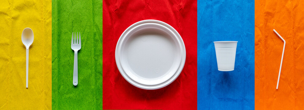 Varios utensilios de una vajilla de pl&aacute;stico blanco desechable sobre fondos de colores.