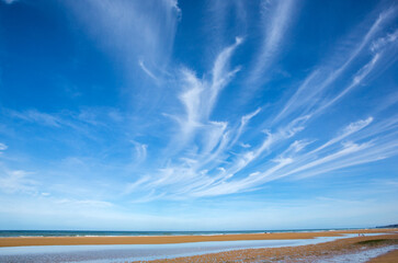 Beach view during the tide with cirrus clouds above. - obrazy, fototapety, plakaty