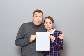 Portrait of adult couple holding together white blank paper sheet