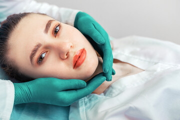 Hands of a beautician around the face of the patient, care about the appearance, beauty, anti-aging procedures.