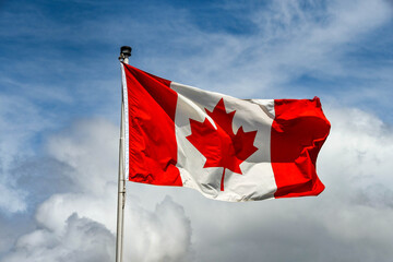 Canadian national flag, the "Maple Leaf", isolated against a blue sky with white clouds. No people.