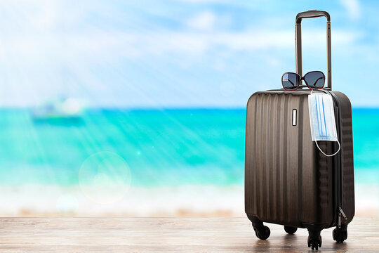 Concept of travel during pandemic . Suitcase with protection mask on the beach