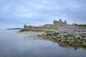 Coastline with pebbles & boulders and the Sandsayre Pier on a grey summer day, Sandwick, Shetland Islands, Scotland.