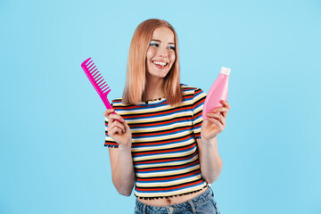 Image of joyful charming girl holding shampoo and comb while smiling