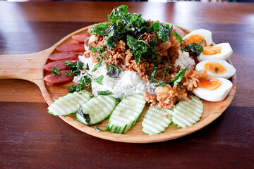 The cropped shot view of Rice topped with stir-fried pork , shimp, Boiled eggs, cucumber and basils on the wood table.