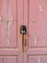 Rusty padlock on pink wooden door with uncorked paint. Old metal padlock on a uncorked wooden door. Old pink door with rusty and spoiled paint.