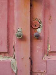 Close-up of broken and uncorked pink wooden door entrance with round door knobs. Old pink door with...