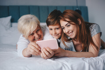 Mother, daughter and grandson looking at the phone together in bed